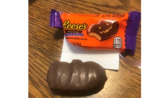 A picture of a Reese's candy wrapper with an illustration that shows a chocolate pumpkin with a carved face, but the candy also shown in the photo has no carving at all.