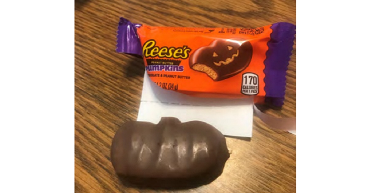 A picture of a Reese's candy wrapper with an illustration that shows a chocolate pumpkin with a carved face, but the candy also shown in the photo has no carving at all.