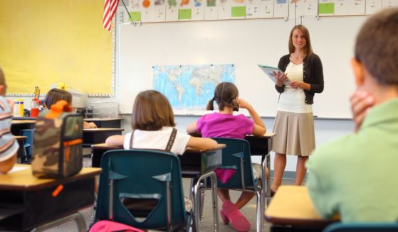 A teacher stands in front of a class in the above stock image.