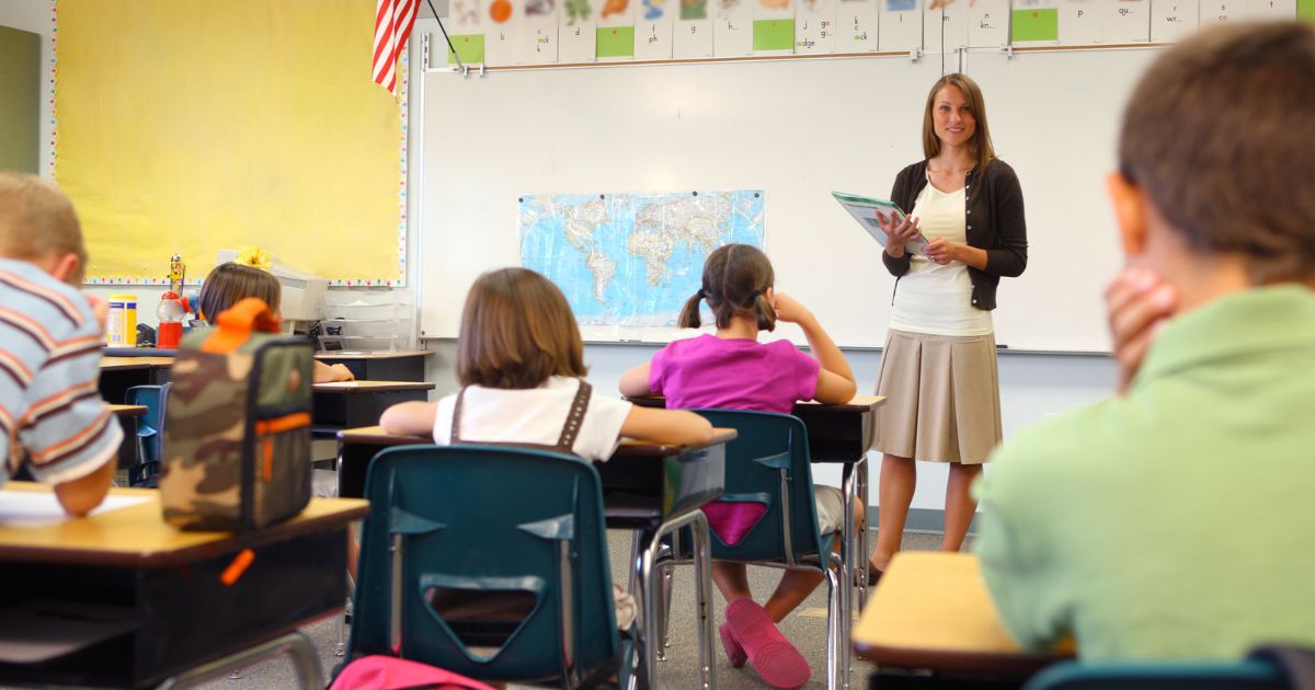 A teacher stands in front of a class in the above stock image.