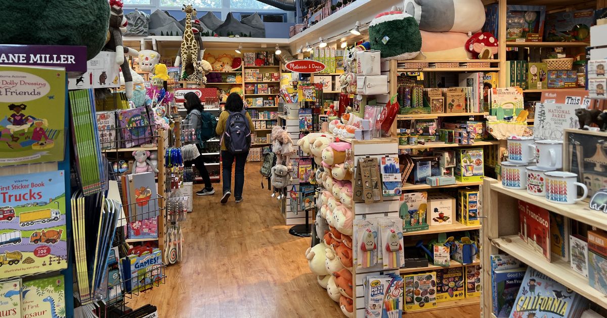 Five Little Monkeys toy store interior, with shelves full of colorful toys, games, books, and plushies, with two warmly dressed female customers near the end of an aisle and silver HVAC ducts on the ceiling, Lafayette, California, October 28, 2022.