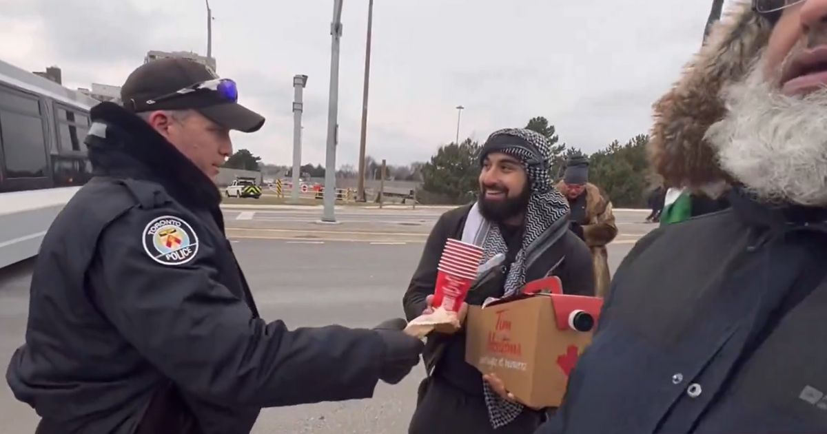 A Toronto police officer delivers coffee to anti-Israel protesters.