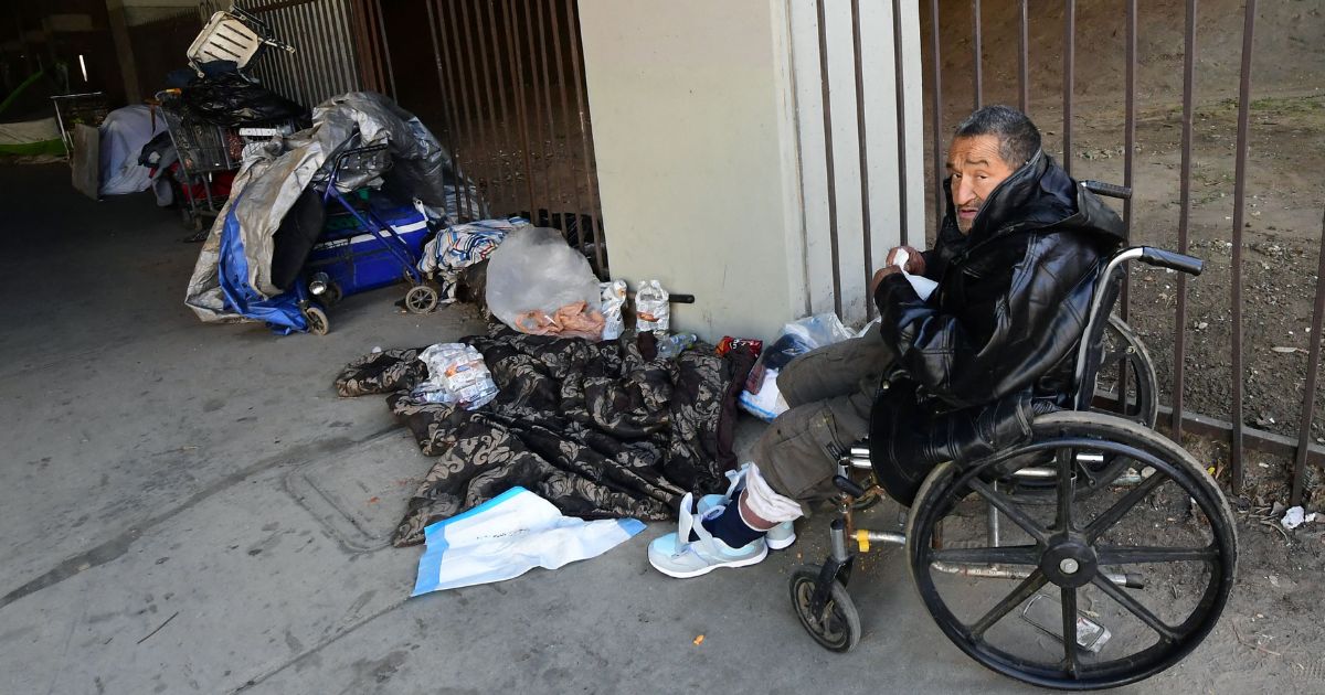 A man sits in his wheelchair at a homeless encampment beneath a freeway overpass near SoFi Stadium in Inglewood, California, on Jan. 26, 2022.