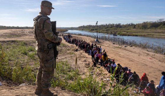 A Texas National Guard soldier watches over a group of more than 1,000 migrants who had crossed the Rio Grande from Mexico on Dec. 18, in Eagle Pass, Texas.