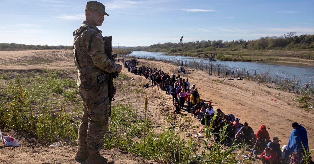 A Texas National Guard soldier watches over a group of more than 1,000 migrants who had crossed the Rio Grande from Mexico on Dec. 18, in Eagle Pass, Texas.