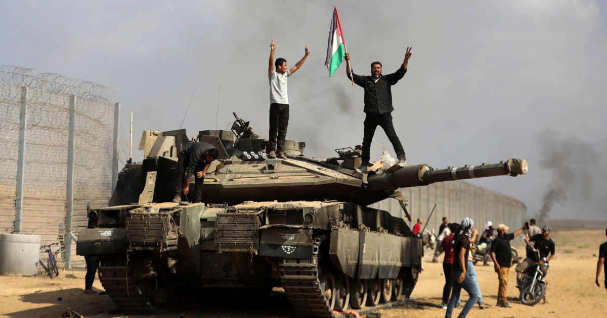 Palestinians wave their national flag and celebrate by a destroyed Israeli tank at the Gaza Strip fence east of Khan Younis on Oct. 7.