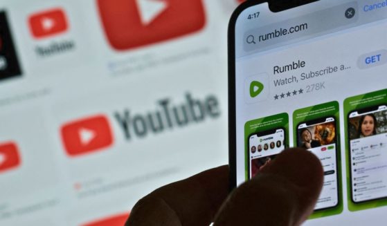 A photo illustration shows the Rumble app download page on a smartphone against a YouTube logo background in Los Angeles on March 29.