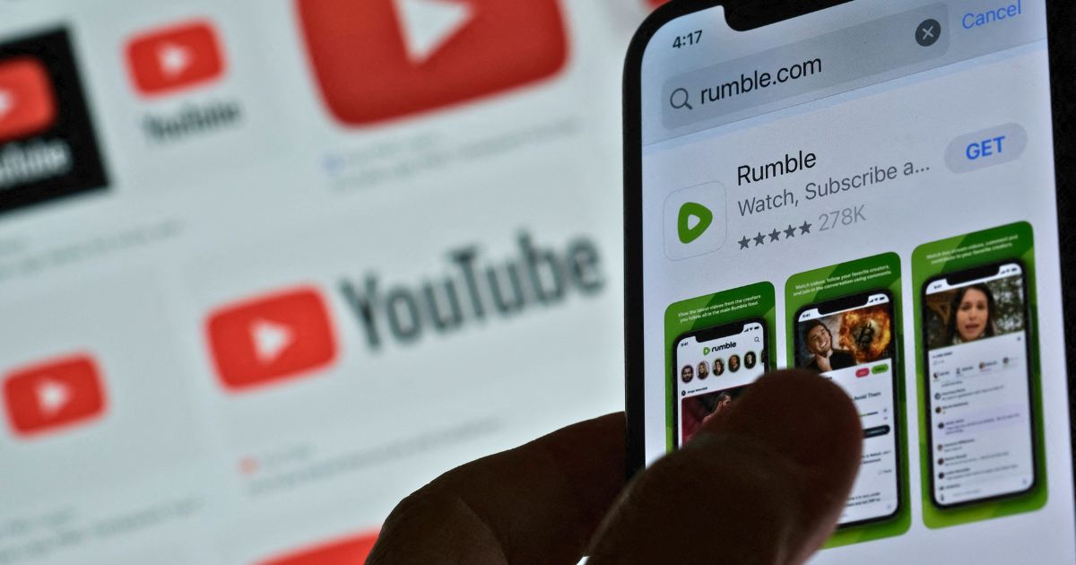 A photo illustration shows the Rumble app download page on a smartphone against a YouTube logo background in Los Angeles on March 29.