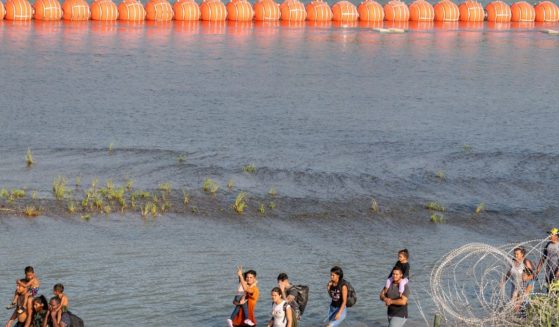Immigrants walk by a string of buoys placed on the water along the Rio Grande border with Mexico in Eagle Pass, Texas, on July 15. The buoys are part of an operation that Texas has used to protect its borders from illegal immigration.