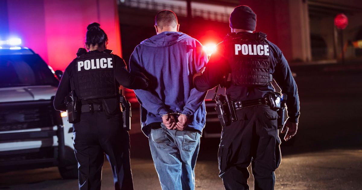 This stock image shows two police officers walking a cuffed man.