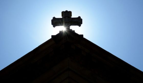 The morning sun rises behind a stone cross atop The Cathedral Basilica of St. Francis of Assisi, commonly known as Saint Francis Cathedral, in Santa Fe, New Mexico.