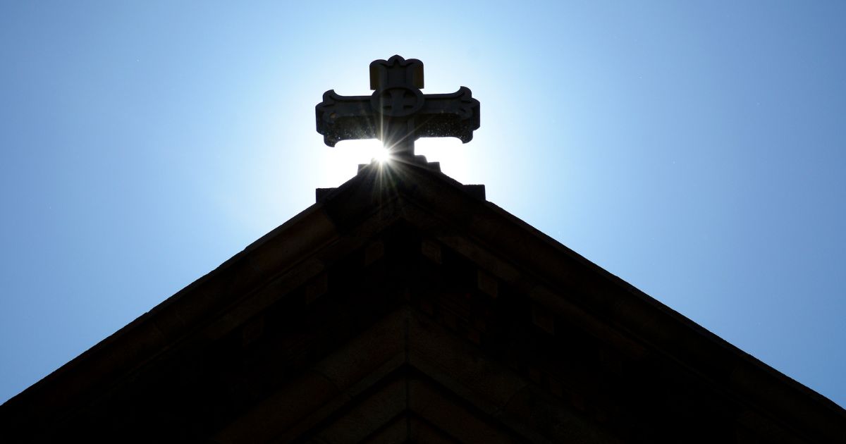 The morning sun rises behind a stone cross atop The Cathedral Basilica of St. Francis of Assisi, commonly known as Saint Francis Cathedral, in Santa Fe, New Mexico.