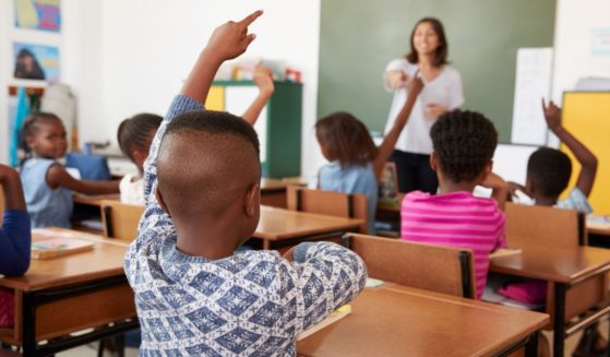 A stock photo shows children raising their hands in a classroom.