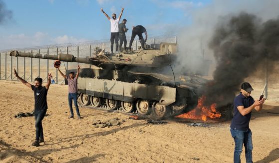 Palestinians celebrate by a destroyed Israeli tank at the Gaza Strip fence east of Khan Younis on Oct. 7.