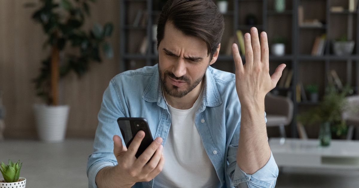 A stock photo shows a man looking frustrated while holding a cellphone.