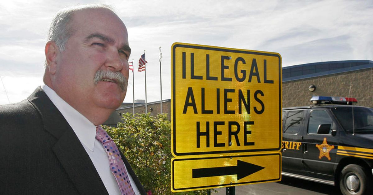 Butler County, Ohio, Sheriff Richard Jones stands next to a sign with an arrow labeled "Illegal Aliens Here" that he had installed in the sheriff's office parking lot in Hamilton, Ohio.