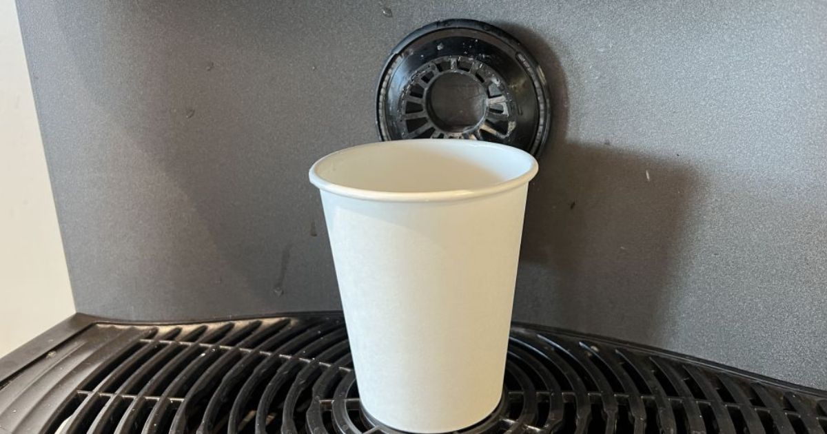 A paper cup is shown on a commercial coffee machine.