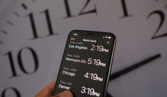 A clock in the background of a smartphone showing the time after Daylight Saving Time was implemented in Los Angeles on March 15, 2022.