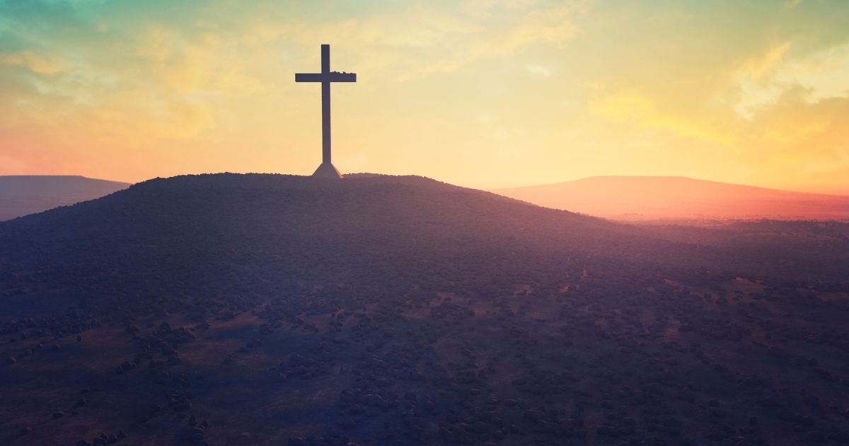 A cross is shown on a hill in the desert.
