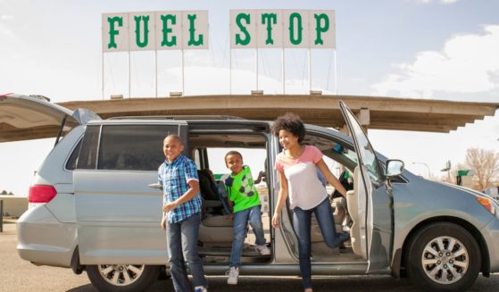 This stock image shows a family getting out of their gas-powered minivan at a gas station.