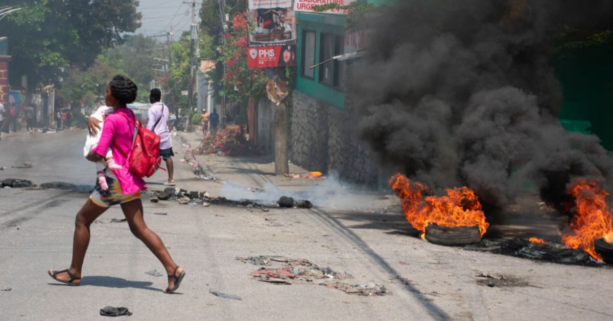 A woman carrying a child runs from the area after gunshots were heard in Port-au-Prince, Haiti, on March 20.