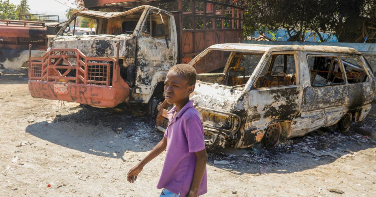 A youth walks by charred cars outside a police station set on fire by armed gangs in Port-au-Prince, Haiti, on Tuesday.