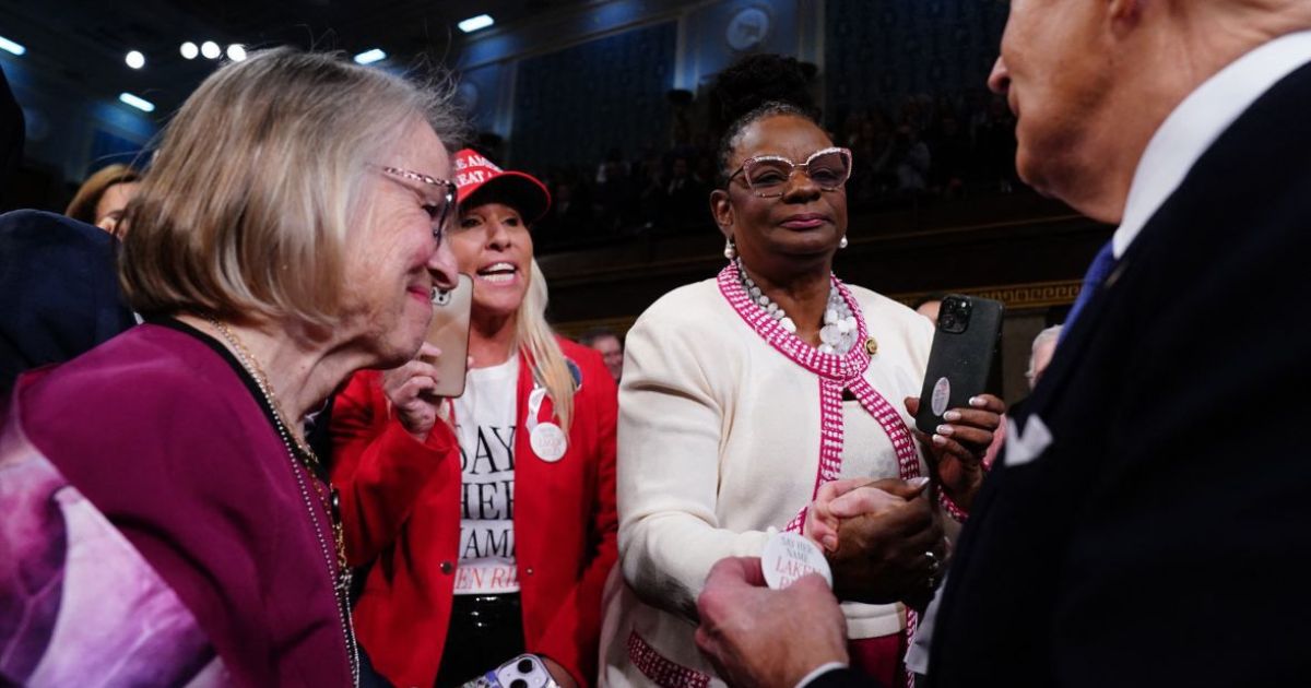 Rep. Marjorie Taylor Greene, center left, hands President Joe Biden, right, a button with 22-year-old murder victim Laken Riley’s name on it as he walks into the House of Representatives chamber to give the State of the Union address Thursday night.