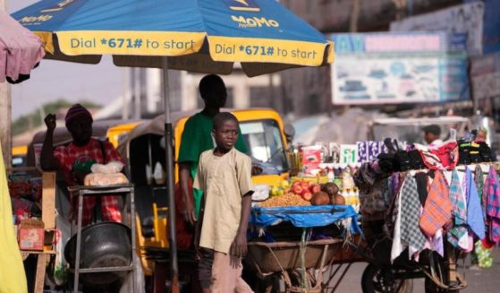 A boy walks past people selling on the street in Kaduna, Nigeria, on Friday. Security forces swept through large forests in Nigeria's northwest region on Friday in search of nearly 300 children who were abducted from their school a day earlier.