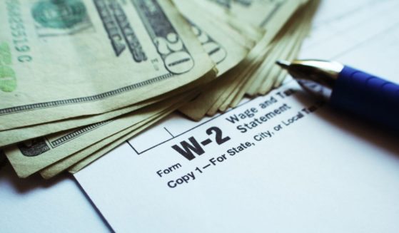 This stock image shows a stack of cash next to a W-2 form.