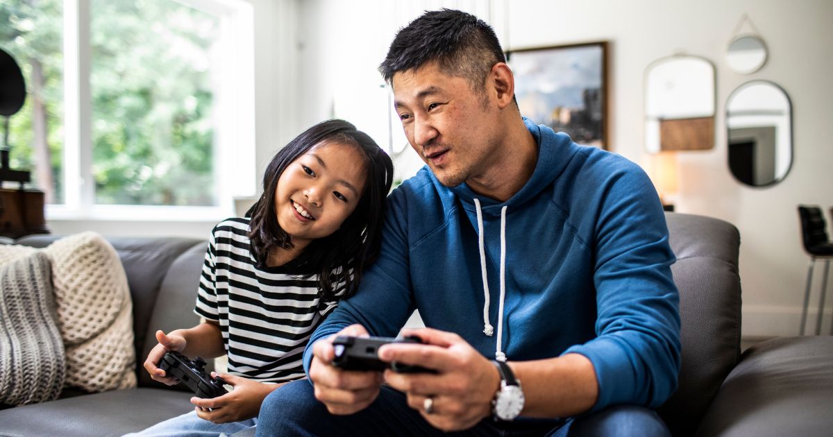 This stock image shows a father and daughter playing video games.