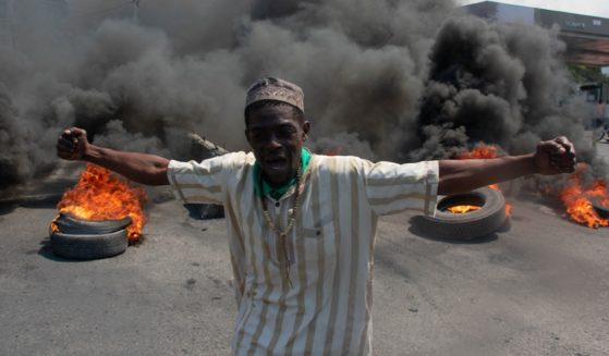 A Haitian man screams as tires burn in the background at a demonstration Tuesday in Port-au-Prince, Haiti.