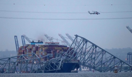 a helicopter flying over the container ship Dali as it rests against wreckage of the Francis Scott Key Bridge