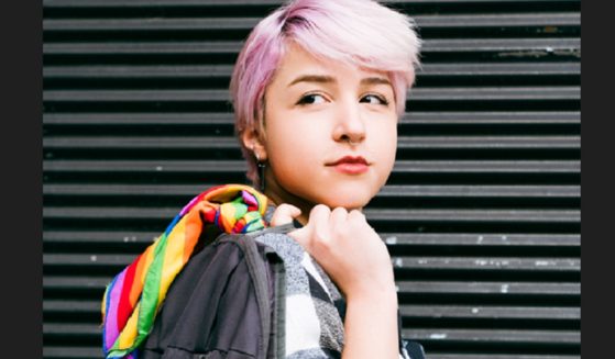 A young person of indeterminate gender with pink hair looking pensive.
