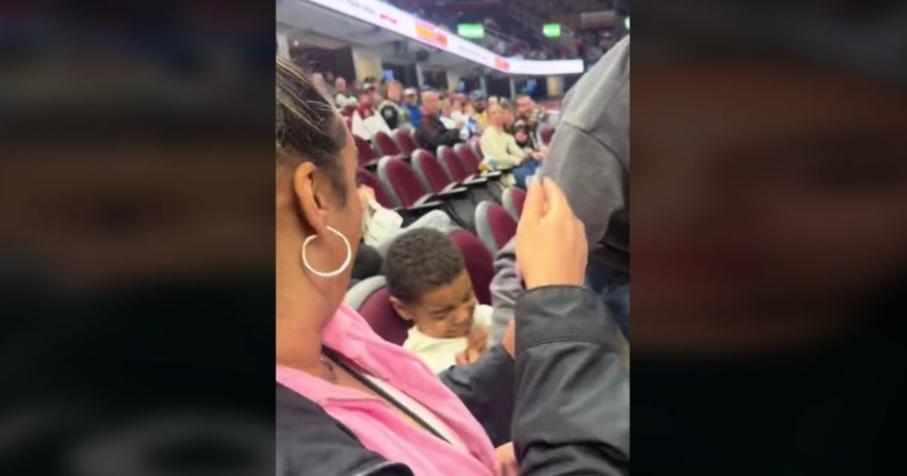 a mother looking on as a man sitting next to her son at a hockey game intercepts a puck that might have hit him