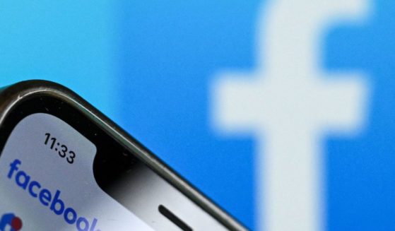 The logo of Facebook on the screen of a smartphone with another Facebook logo out of focus in the background.