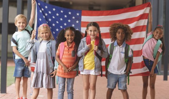 This stock image shows a group of elementary students standing proudly with an American flag.