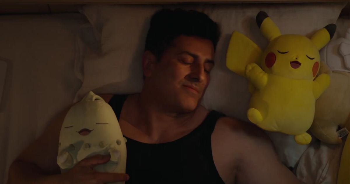 A man in a tank top cuddles up to two Pokémon plushies.