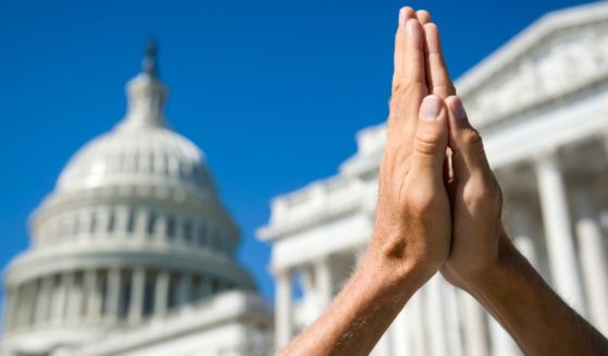 This picture shows hands held together in prayer in front of U.S. Capitol Building in Washington, D.C.
