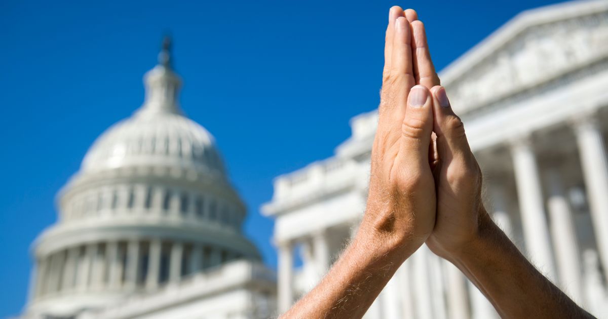 This picture shows hands held together in prayer in front of U.S. Capitol Building in Washington, D.C.