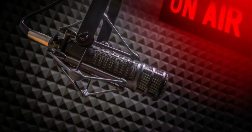 This image shows a professional microphone in a radio station studio with an on air sign.