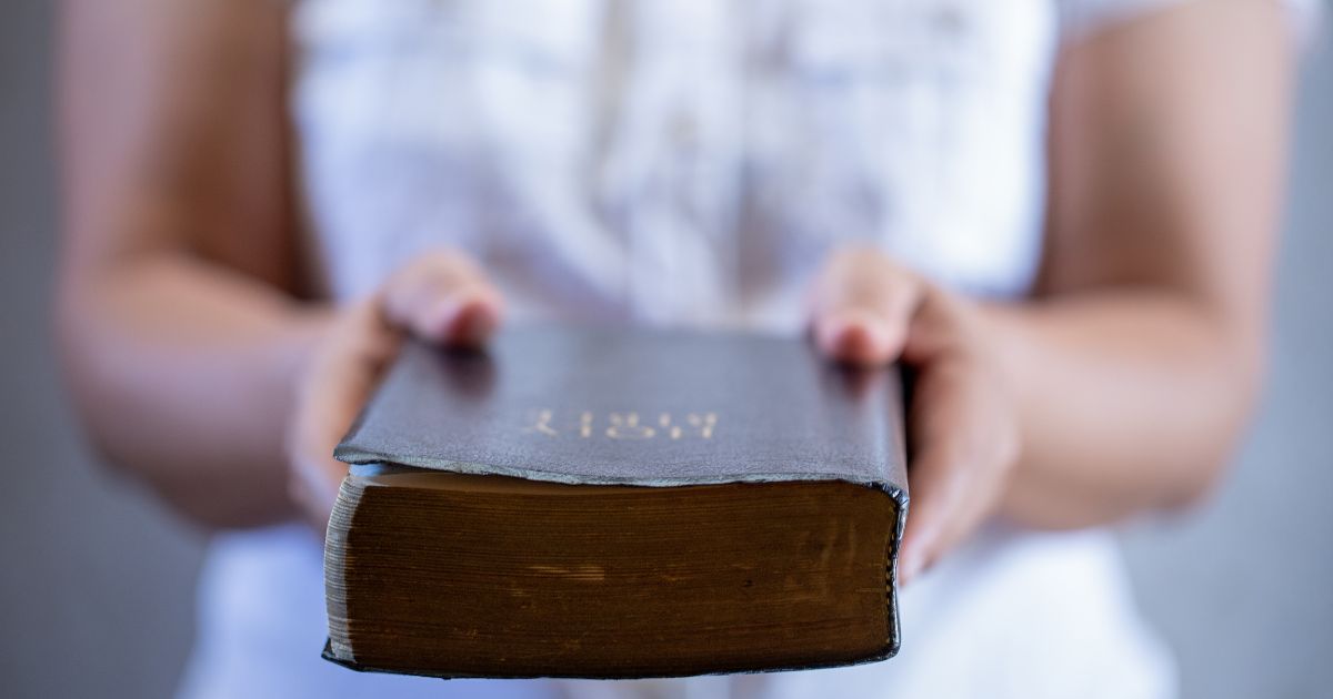 In this photo, a woman is holding out a Bible, offering it to anyone who would like to read it.