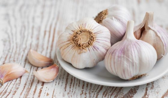 Four garlic bulbs are sitting on a white plate with 3 cloves of garlic next to them.