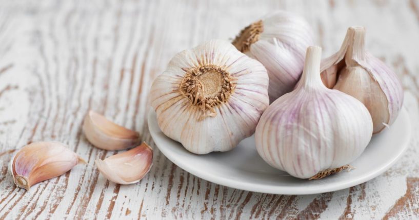 Four garlic bulbs are sitting on a white plate with 3 cloves of garlic next to them.