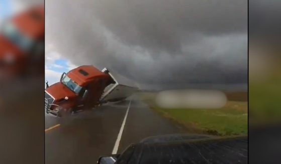 winds near a tornado blowing a semi truck over in front of a storm chaser