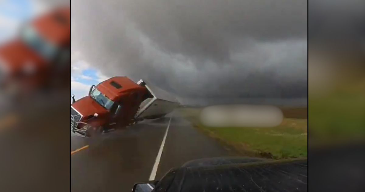 winds near a tornado blowing a semi truck over in front of a storm chaser