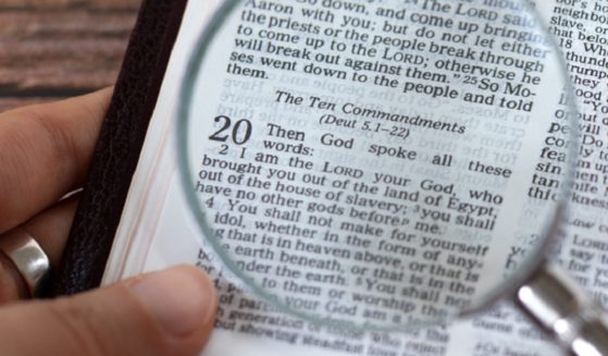 A man's hand holds a magnifying glass over a Bible chapter heading for "The Ten Commandments."