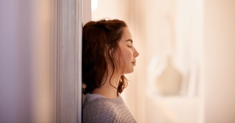 This image shows a young woman leaning her back against a wall while shutting her eyes.