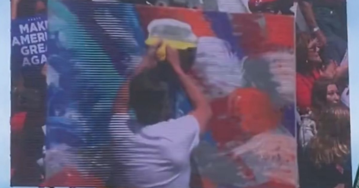 An artist painting the US flag at a Trump rally starts peeling the middle of the artwork, causing a wild reaction from the crowd as they realize what’s happening