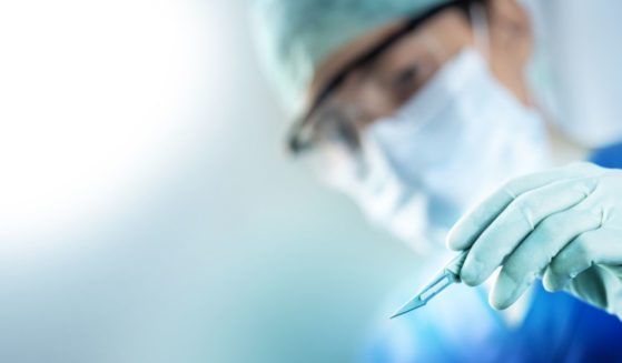 A surgeon's hand holds a scalpel with his face blurred in the background.