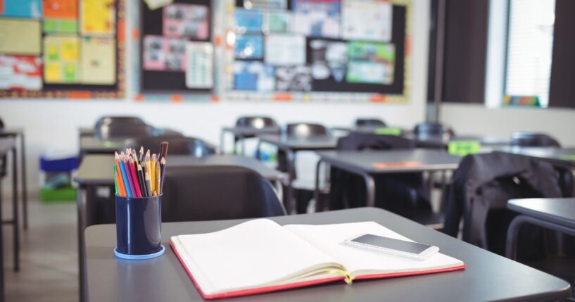 Mobile phone on open book at desk in classroom.